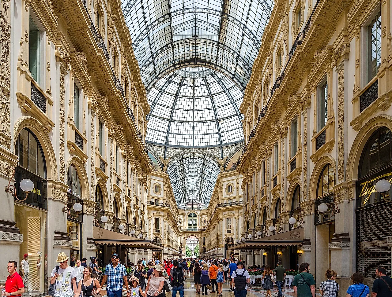 Inside the Galleria Vittorio Emanuele II: the glass-and-iron vault overhead, the ornate facades with arcades on both sides, and crowds of visitors in the foreground.